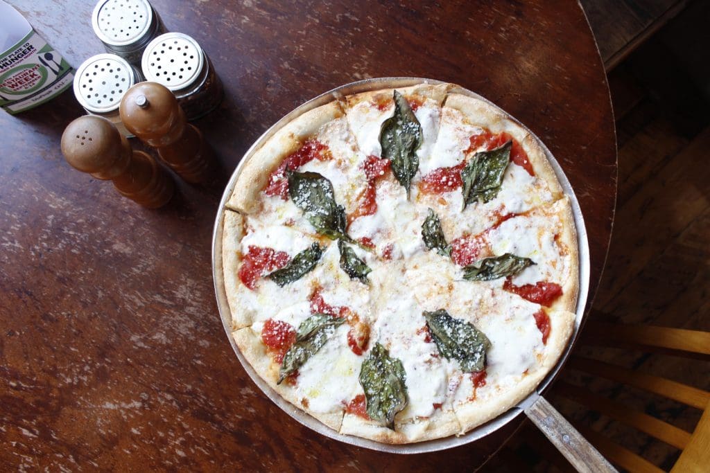 A pizza with basil leaves on top Description automatically generated