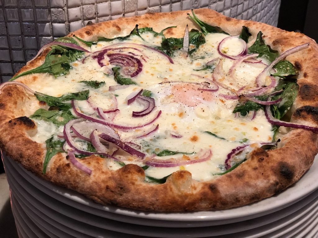 A pizza with onions and spinach on a plate

Description automatically generated