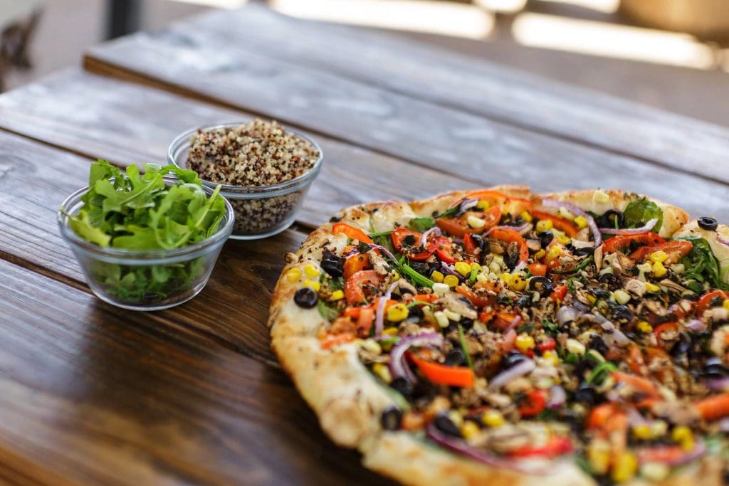 A pizza with vegetables and a bowl of salad

Description automatically generated